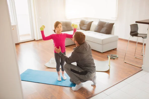 Батько і дочка тренуються вдома. Тренування в квартирі. Спорт вдома. Вони стоять на килимку для йоги. Дівчина тримає гантелі — стокове фото