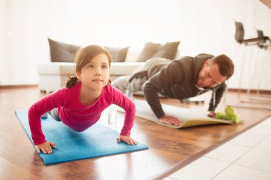 Baba ve kızı evde antrenman yapıyorlar. Apartman dairesinde egzersiz. Evde spor haberleri. Yoga minderlerinde birlikte zemin üzerinde iterler..