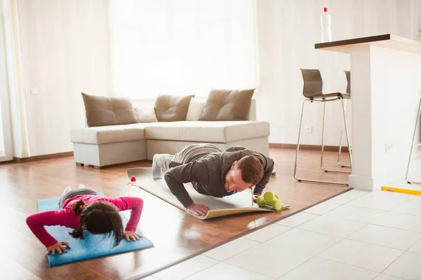 Père et fille s'entraînent à la maison. Entraînement dans l'appartement. Le sport à la maison. Ils poussent sur le sol ensemble sur des tapis de yoga . — Photo