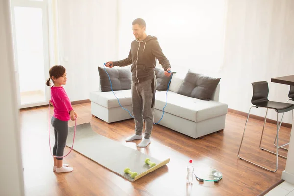 Ojciec i córka trenują w domu. Ćwiczenia w mieszkaniu. Sport w domu. Używają gumowej liny do treningu. — Zdjęcie stockowe