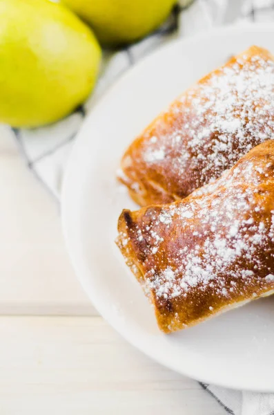 Tarte aux pommes fraîchement cuite sur assiette et deux pommes jaunes fraîches sur fond bois clair et serviette — Photo