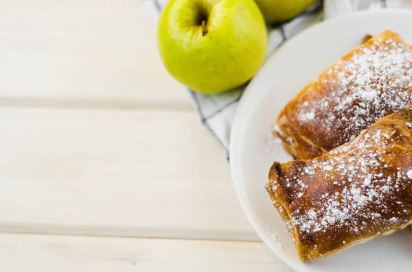 Tarte aux pommes fraîchement cuite sur assiette et deux pommes jaunes fraîches sur fond bois clair et serviette — Photo