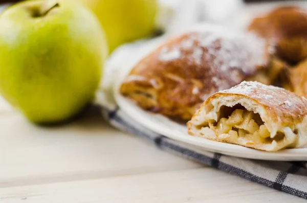 Frisch gebackener Apfelkuchen auf Teller und zwei frische gelbe Äpfel auf hellem Holzhintergrund und Handtuch — Stockfoto