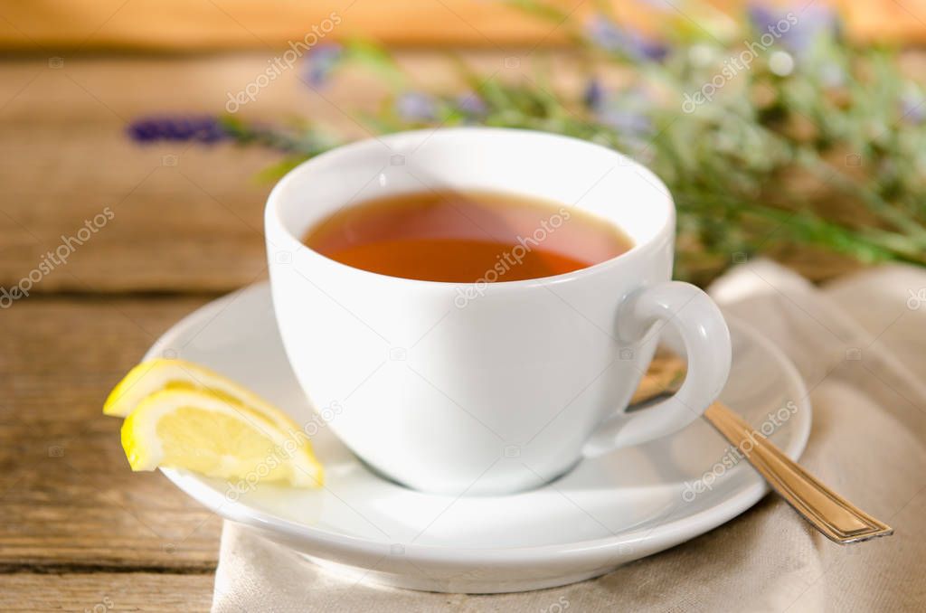 White cup of tea with a saucer, with lemon in the sun is on a wooden table