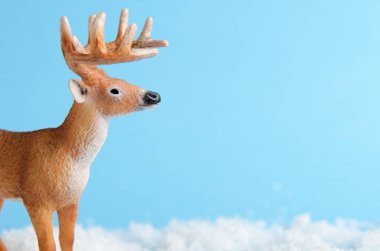 Toy deer on blue background is standing on artificial snow close-up. Background for childrens or winter advertising banner. Copy space