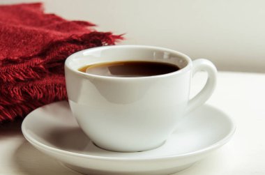 Mug with warm tea on a white table on white background with a red folded warm blanket in the background. Home comfort.