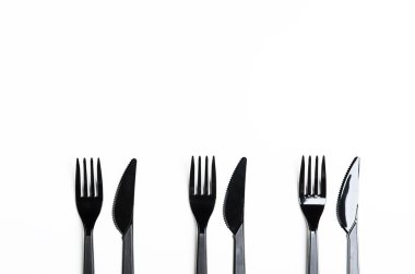 Clean plastic black forks and knives on white background. Disposable dishes, environmental pollution. Copy space, top view, flat lay.
