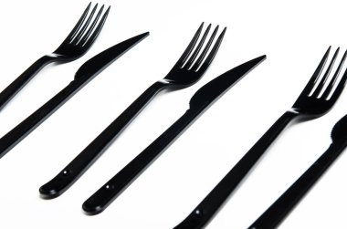 Clean plastic black forks and knives on white background. Disposable dishes, environmental pollution.