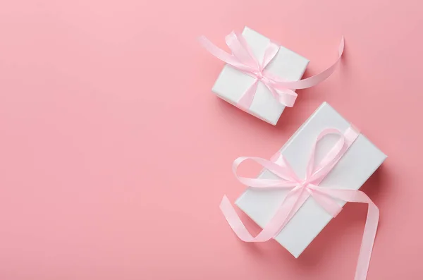 Pembe bir arka planda pembe kurdeleli beyaz hediye kutusu. Doğum günü hediyesi, kadınlar günü ya da Noel. Üst görünüm, boşluk kaydet, düz yat.