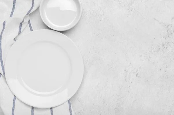 Clean white plates on fresh towel with stripes on a stone light minimalist background. Top view, copy space, flat lay. — Stock Fotó
