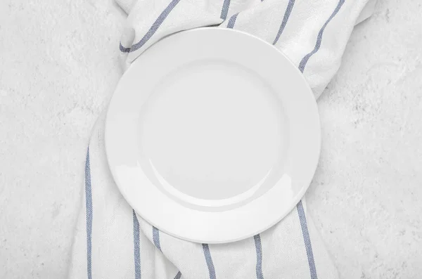 Clean white plate on fresh towel with stripes on a stone light minimalist background. Top view, flat lay. — Stock Fotó