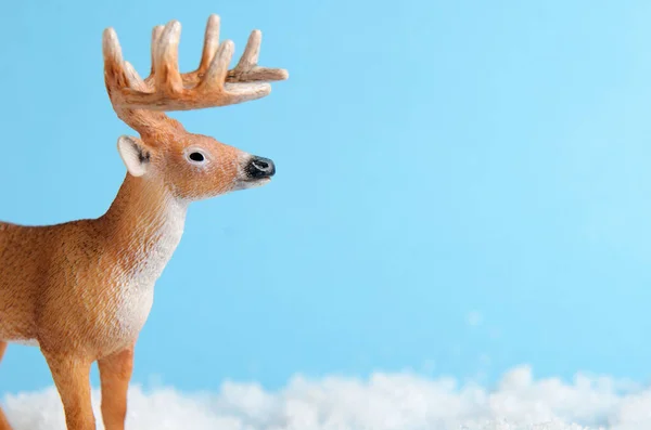 Toy deer on blue background is standing on artificial snow close-up. Background for childrens or winter advertising banner. Copy space — Stockfoto