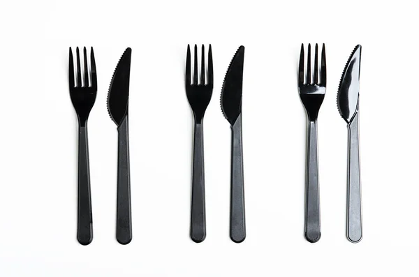 Tiszta műanyag fekete villák és kések fehér háttérrel. Eldobható edények, környezetszennyezés. Felülnézet, lapos fektetés. — Stock Fotó