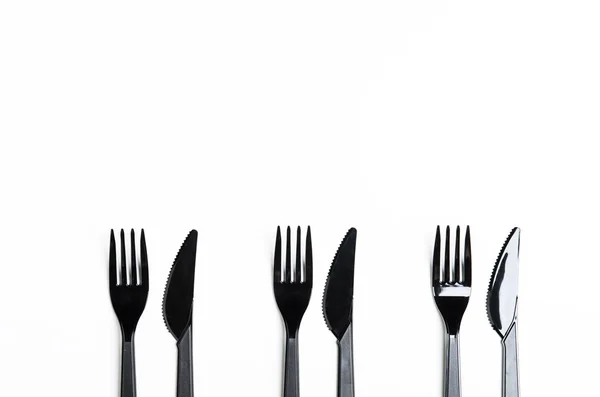 Cuchillos y tenedores negros de plástico limpio sobre fondo blanco. Platos desechables, contaminación ambiental. Copiar espacio, vista superior, plano . — Foto de Stock