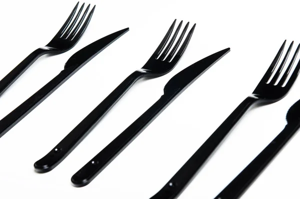 Clean plastic black forks and knives on white background. Disposable dishes, environmental pollution. — Zdjęcie stockowe