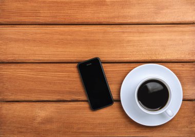Koyu ahşap arka planda bir fincan sıcak kahve ve bir cep telefonu. Boşluğu kopyala, üst görünüm, düz uzanma