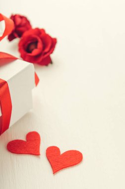 Beyaz hediye kutusu, beyaz arka planda kırmızı bir kurdele, çiçekler ve kumaştan iki kalp. Sevgililer Günü konsepti, kadınlar günü..