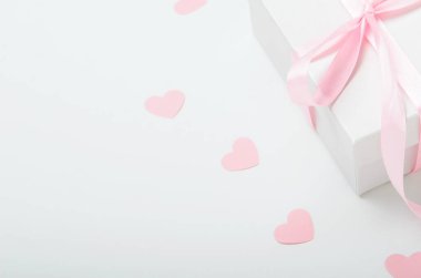 Pembe kurdeleli beyaz hediye kutusu ve beyaz arka planda kalpler. Sevgililer günü hediyesi, kadınlar günü. Boşluğu kopyala.