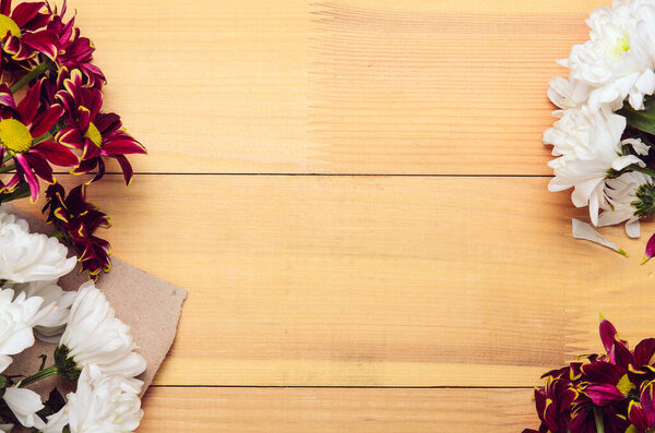 Frame of white and red chrysanthemum flowers on craft paper. Wooden background, copy space, top view, flat lay.