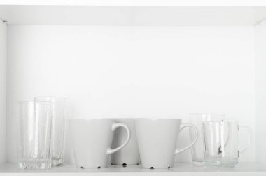 Bardaklar ve bardaklar dolapta beyaz bir rafta. Temiz tabaklar, mutfak aletleri..