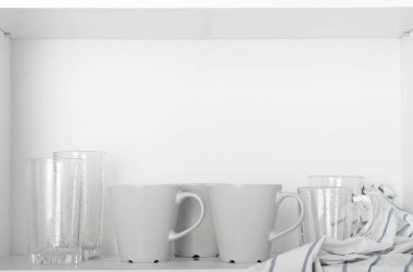 Bardaklar ve kupalar beyaz bir rafta, dolapta temiz bir havluyla. Temiz tabaklar, mutfak aletleri..