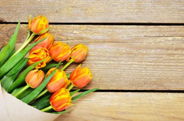 Tahta arka planda Kraft ambalajında bir buket kırmızı-sarı lale. Boşluğu kopyala, üst görünüm, düz uzanma