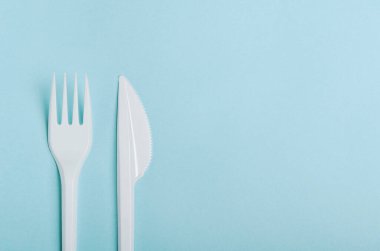 Mavi arka planda plastik, tek kullanımlık çatal ve bıçak. Plastik tabaklar, fast food, plastik kirliliği saymazsak. Boşluğu kopyala, üst görünüm, düz uzanma.