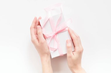 Pembe kurdeleli hediye kutusu olan bir kadın eli. Tatil kavramı, hediye, tebrikler. Üst manzara, düz uzanma