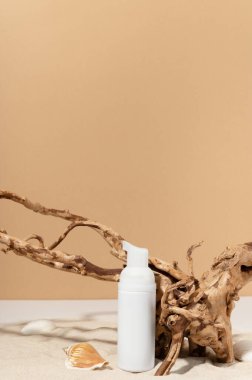 Yumuşak kozmetik köpüklü kap kumun üzerinde deniz kabuğu ve dekoratif ağaç ile duruyor. Fotokopi alanı olan plastik tüp. Sağlık ve organik yüz ürünleri konsepti.