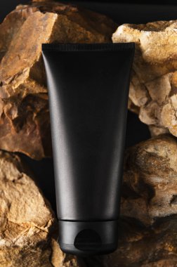 Nemlendirici yüz kremi olan siyah markasız tüp. Taşların arkasındaki flakon. Model stili, dikey resim. Profesyonel cilt bakımı ve güzellik. Erkek kozmetik ve sağlık konsepti.