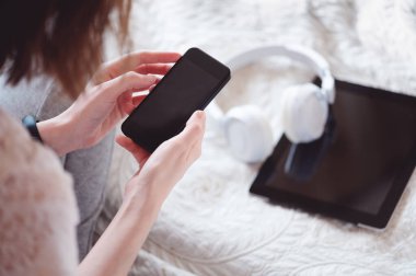 Ekranda fotokopi alanı olan modern akıllı telefonu tutan kadınların üst görüntüsü. Tablet ve kulaklıklar yatağa. Evde aletlerle, aletlerle, modern yaşam tarzıyla vakit geçirmek..
