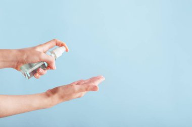 Virüs ve mikrop bulaşmasını önlemek için alkol ya da anti bakteri spreyi kullanan biri. Kişisel hijyen ve dezenfektan jeli konsepti. Model stili. Sağ tarafta uzayı kopyala. Mavi üzerine izole edilmiş..