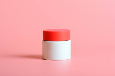 Pembe arka planda kırmızı kapaklı beyaz kavanozda yüz kremi. Kozmetik, güzellik. En düşük bileşim