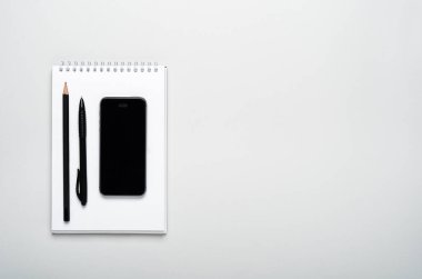 Akıllı telefon, kalem, gri arka plandaki not defterine kalem. Ofis masaüstü, minimum kompozisyon. Boşluğu kopyala, üst görünüm, düz uzanma