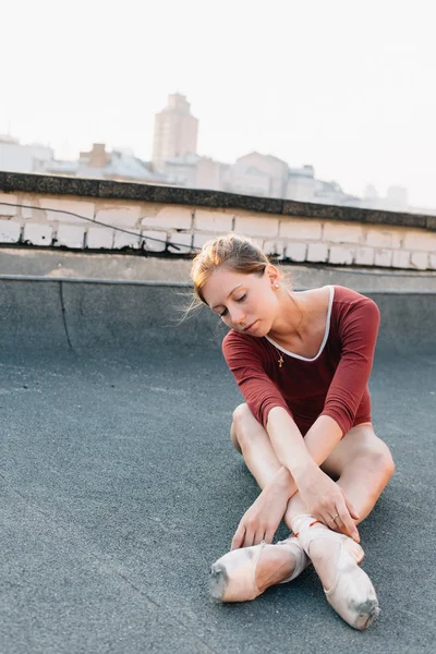 年轻而优雅的芭蕾舞演员在日落时分坐在城市建筑的屋顶上 系着点滴鞋 — 图库照片