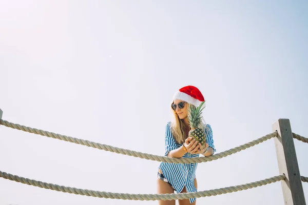 Piękna Młoda Kobieta Blonde Ananasem Pozowanie Santa Hat Przeciw Błękitne — Zdjęcie stockowe