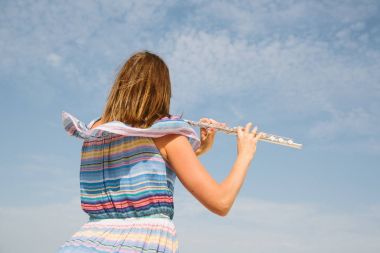 young beautiful woman playing the flute against blue sky  clipart