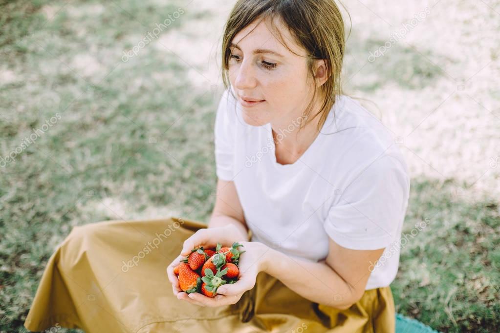 young brunette woman eating fresh strawberries at picnic