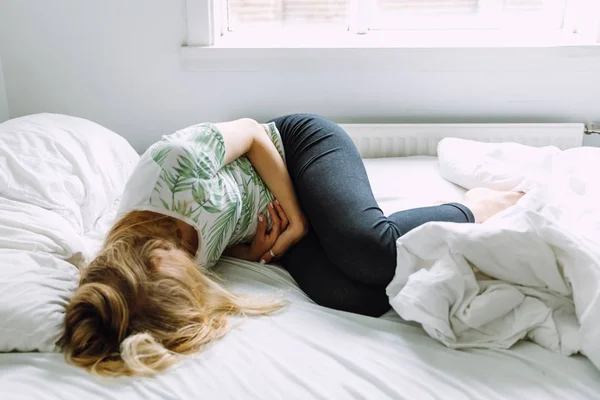 Žena leží na posteli a bolí ji břicho — Stock fotografie
