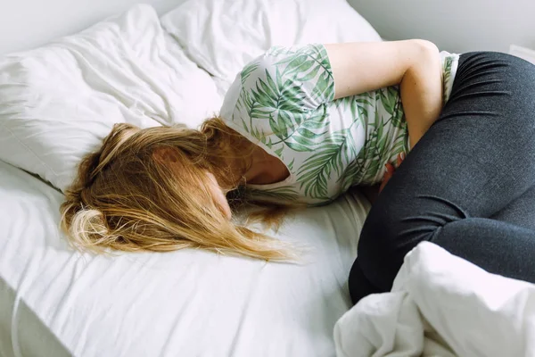 Mulher deitada em uma cama e com dor de estômago — Fotografia de Stock