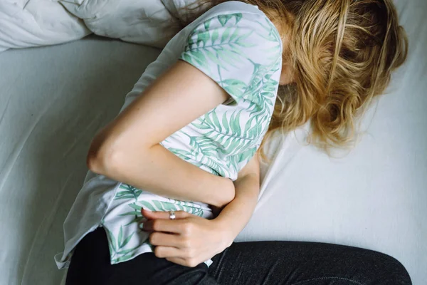 Mujer acostada en una cama y con dolor de estómago — Foto de Stock
