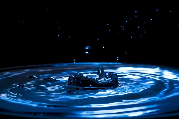 Sprays, druppels, plonsen van het water op een kleurrijke achtergrond — Stockfoto