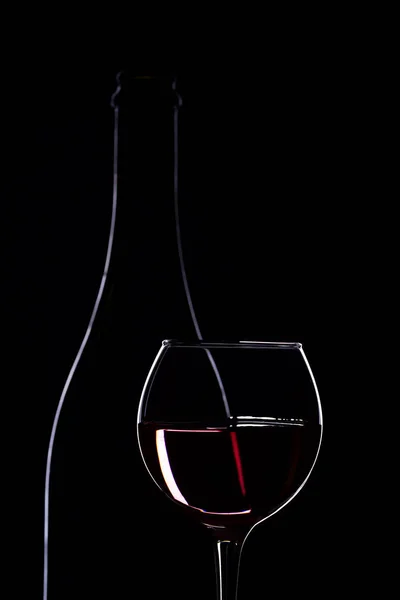 Ποτήρι κρασιού με μπουκάλι κρασί σε μαύρο φόντο, μινιμαλισμό, — Φωτογραφία Αρχείου