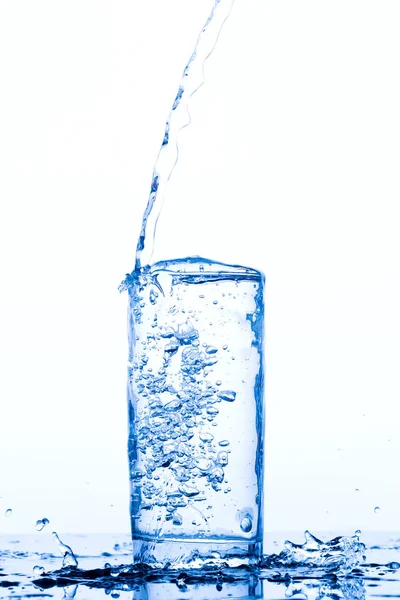 Glas mit eingießendem Trinkwasser Stockbild