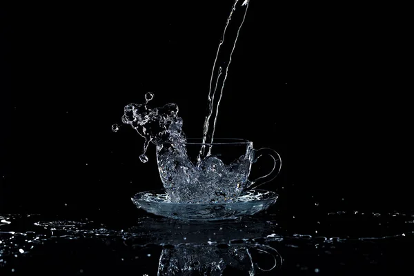 El agua vierte en la taza sobre un fondo negro, luz de estudio —  Fotos de Stock