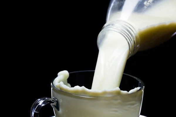 Milch ergießt sich in Glaswaren auf schwarzem Hintergrund — Stockfoto