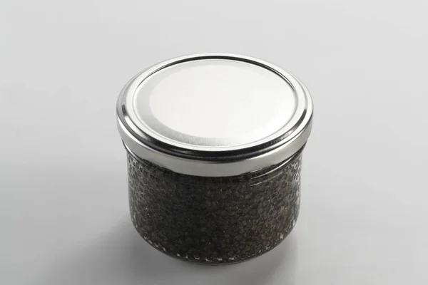 Caviar preto em um frasco em um fundo neutro — Fotografia de Stock
