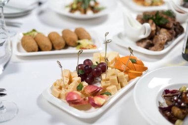 Ziyafet menüsü. Beyaz bir masa örtüsünde dilimlenmiş meyve ve peynir.