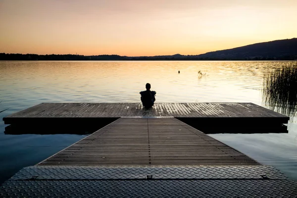 Günbatımı ve Gölü izlerken bir ahşap platform üzerine oturan adam 