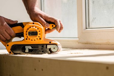 Marangozun elleri arka planda zımpara makinesi tutuyor.